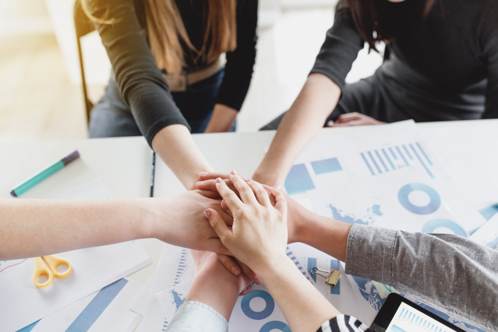 Equipo colaborando con manos unidas sobre documentos de trabajo